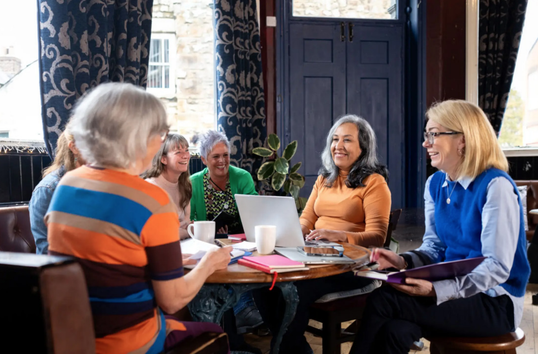 Six women laughing together in a coffee shop