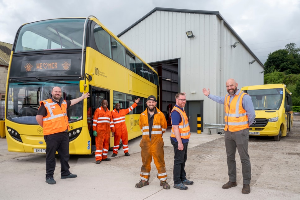 A group standing in front of a bus garage warehouse point towards the garage.